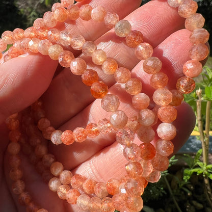 Sonnenstein Tansania | 4mm facettiert | Strang in der Hand | Sonnenlicht | transparentes Pfirsichorange | Happy Minerals