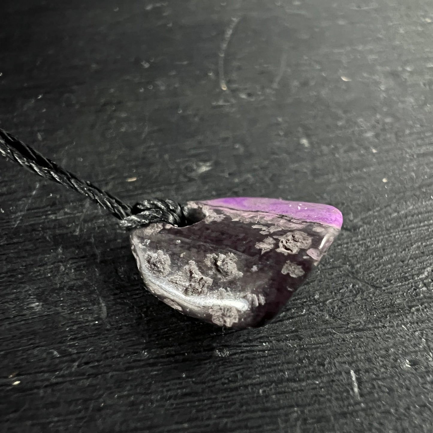 Sugilith Anhaenger, dunkles Violett-Grau mit rosa Zone, raue Textur, an schwarzer Kordel | Happy Minerals