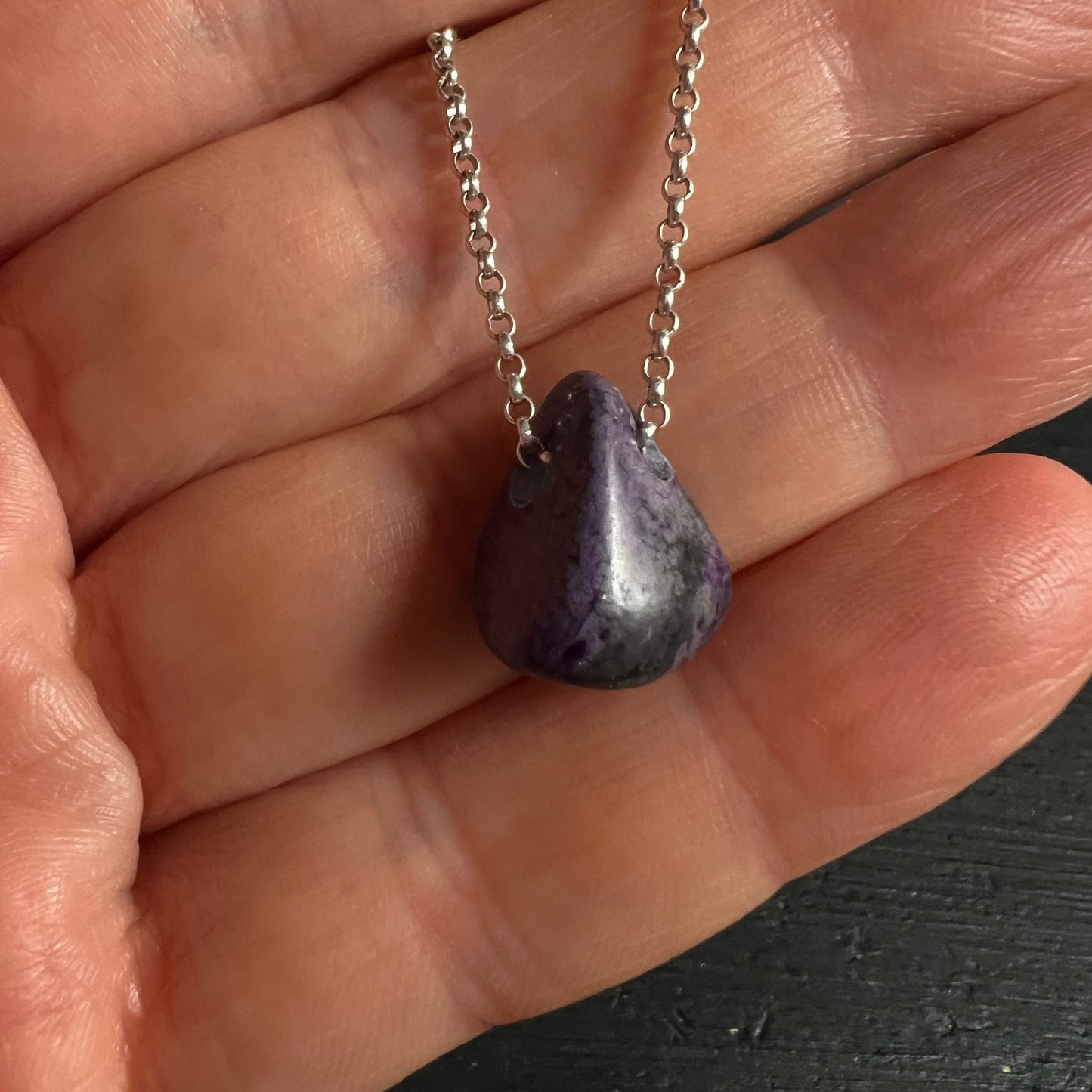 Sugilith Anhaenger tropfenfoermig poliert, violett-grau marmoriert an Silberkette in Hand | Happy Minerals