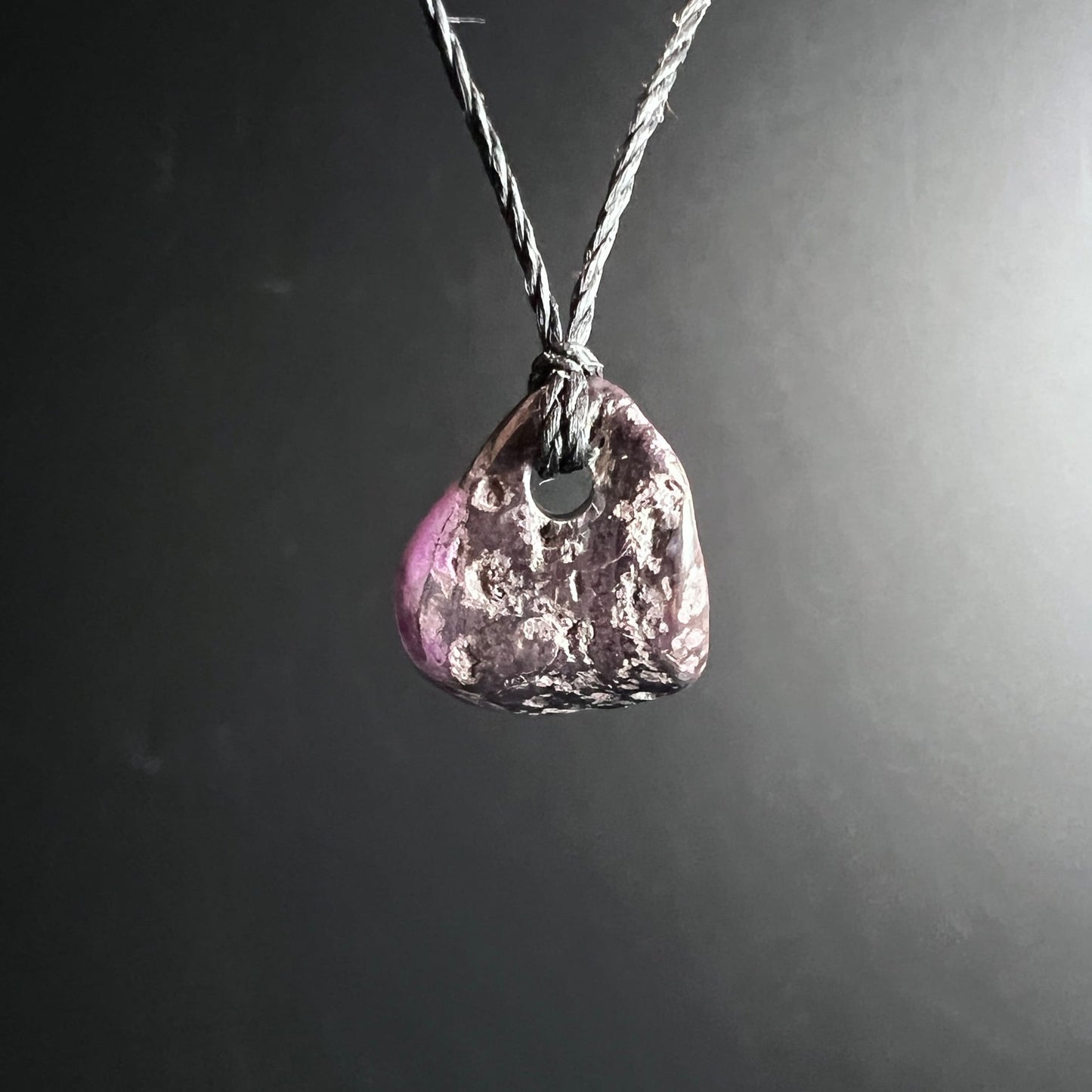 Sugilith Anhaenger, dreieckige Form, dunkles Violett mit rosa Zone und weissen Einschluessen, an Kordel | Happy Minerals