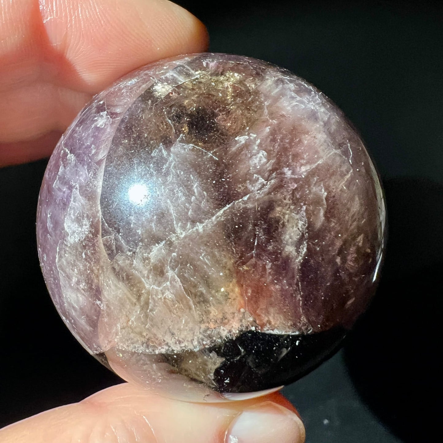Super Seven Kugel in Fingern gehalten | lila-graue Marmorierung | Lichtreflexe | Happy Minerals | Unikat