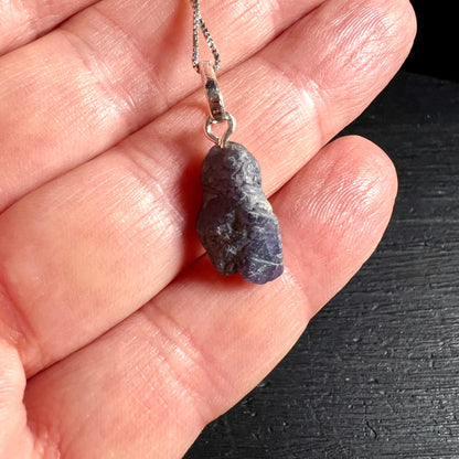 Roher Tansanit Anhaenger in graublau-violett mit weissen Schlieren, an Silberoese, auf Hand fotografiert | Happy Minerals