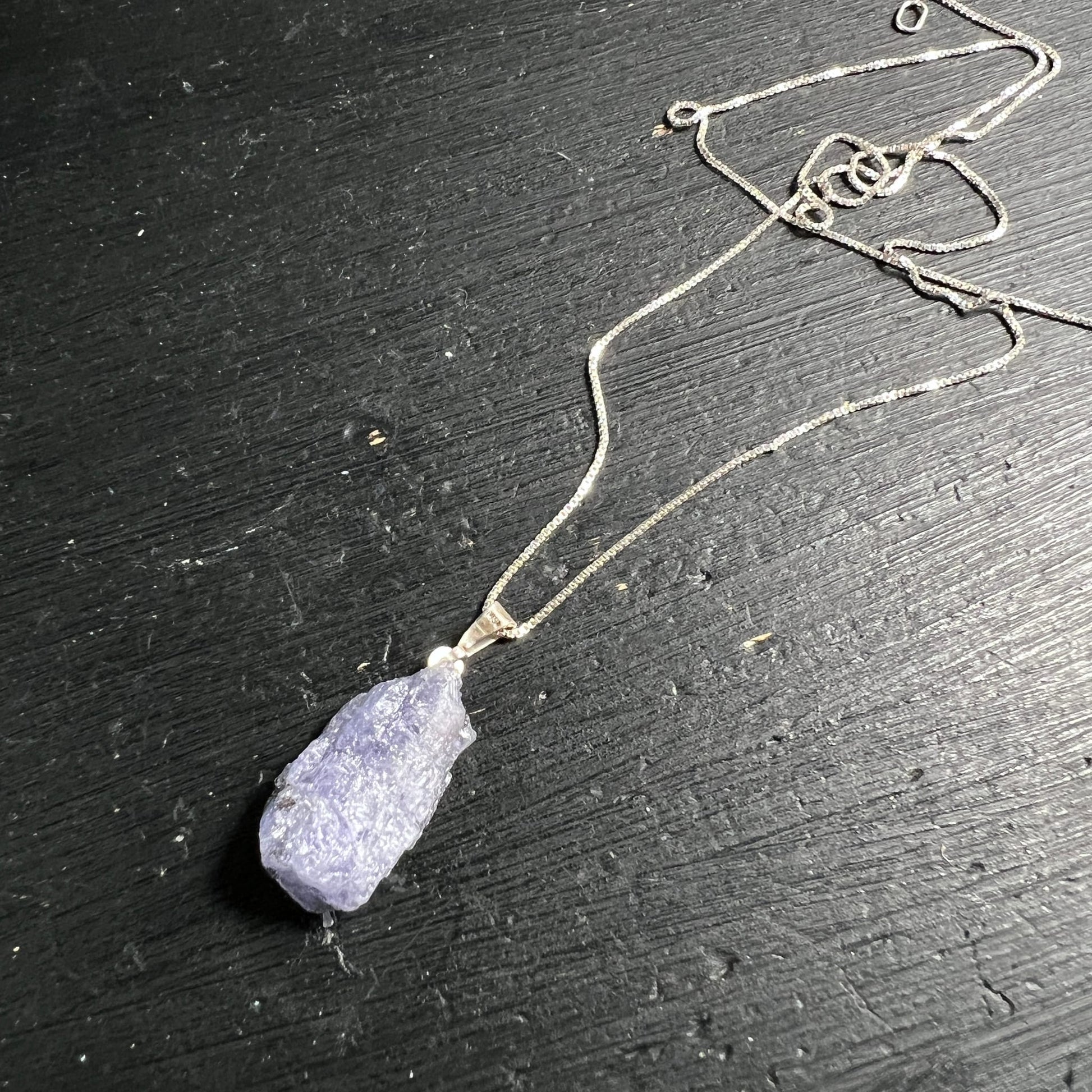 Tansanit Rohstein | blau-violett | 925 Silberkette | liegend auf schwarzem Holz | Unikat | Happy Minerals