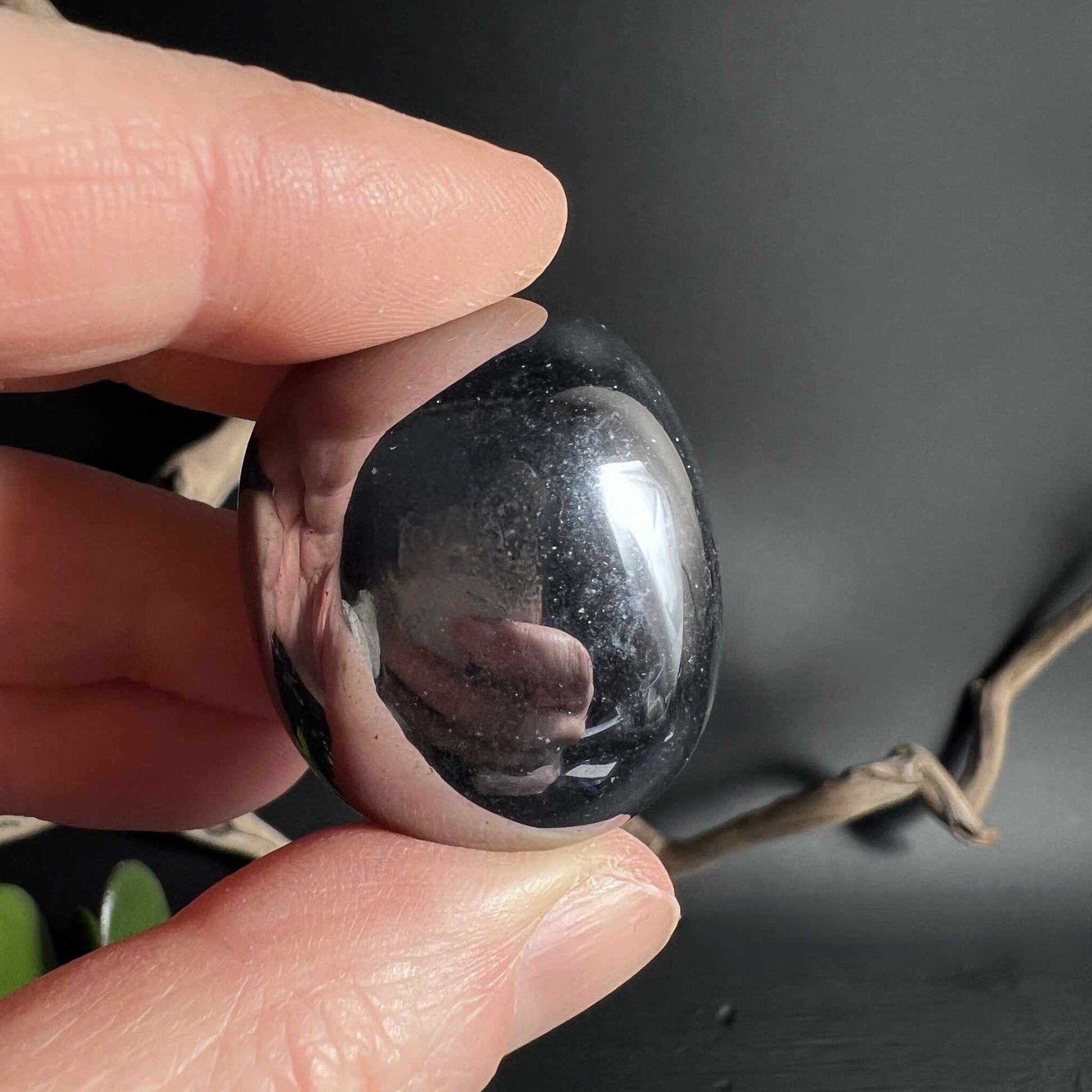 Terahertz Trommelstein ruht zwischen Fingern tiefschwarz mit Lichtspiel | Happy Minerals