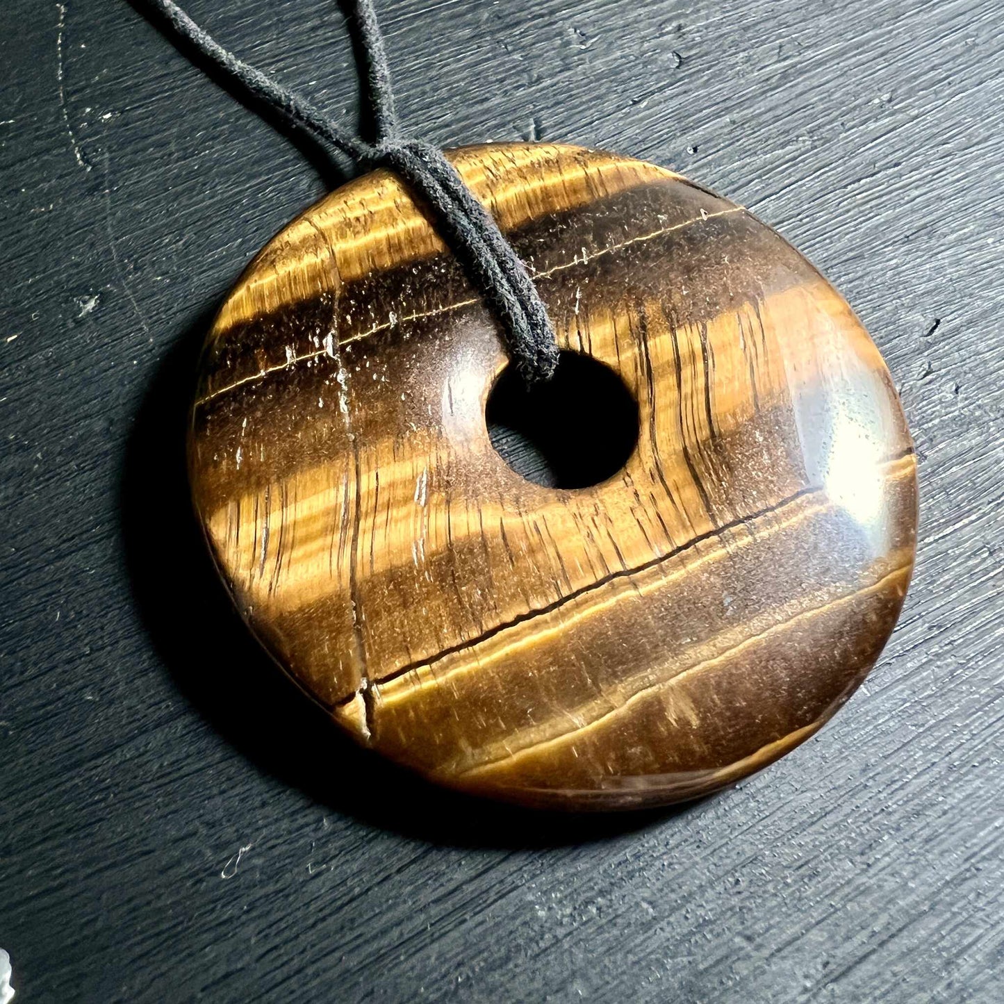 Tigerauge Donut Anhänger mit seidiger Goldstreifung auf schwarzem Hintergrund