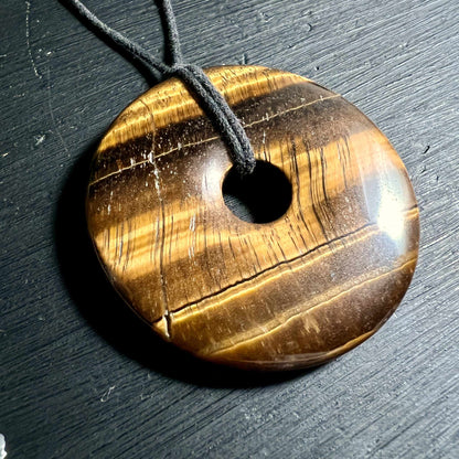 Tigerauge Donut Anhänger mit seidiger Goldstreifung auf schwarzem Hintergrund