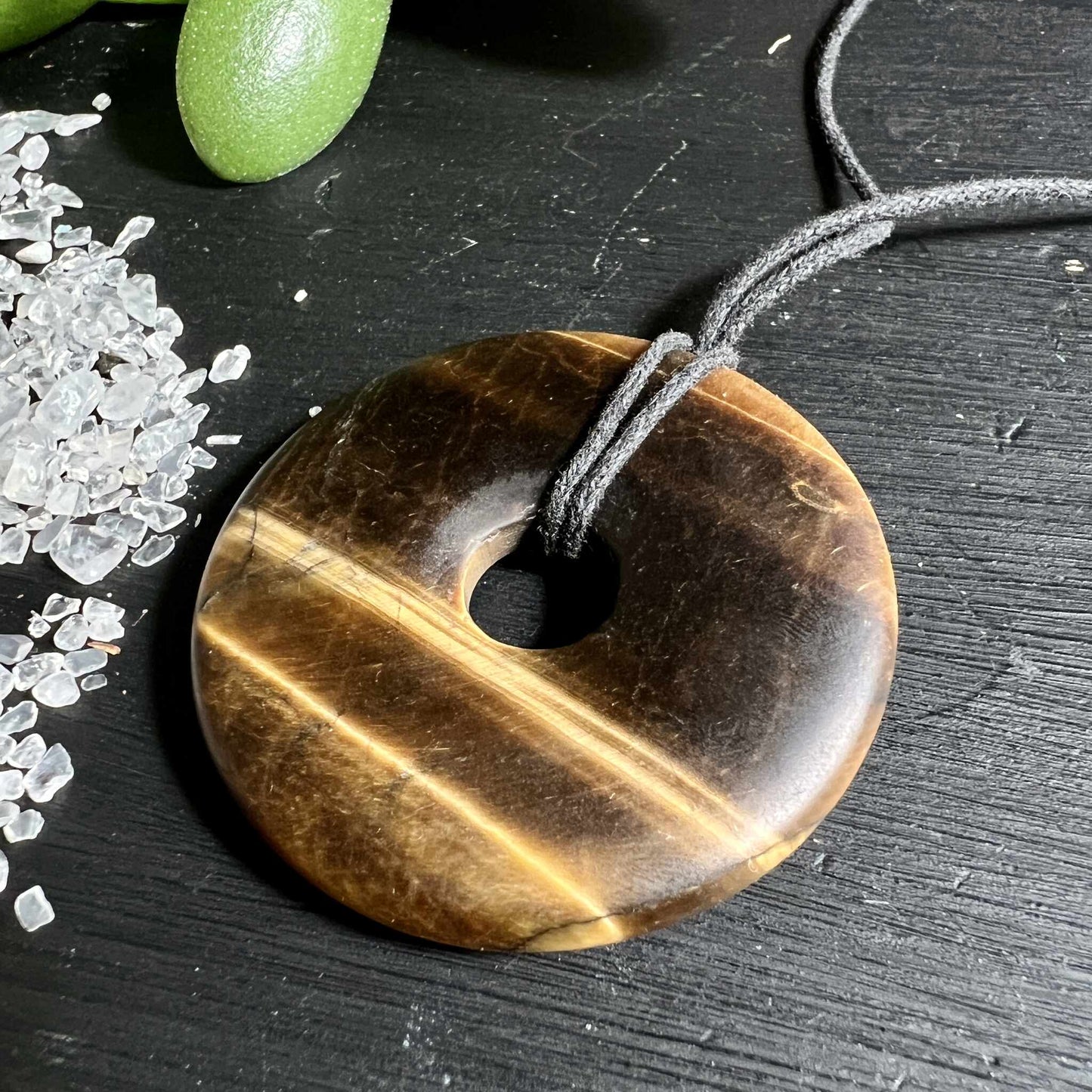 Matter Tigerauge Donut 50mm mit samtiger Oberflaeche neben Bergkristall