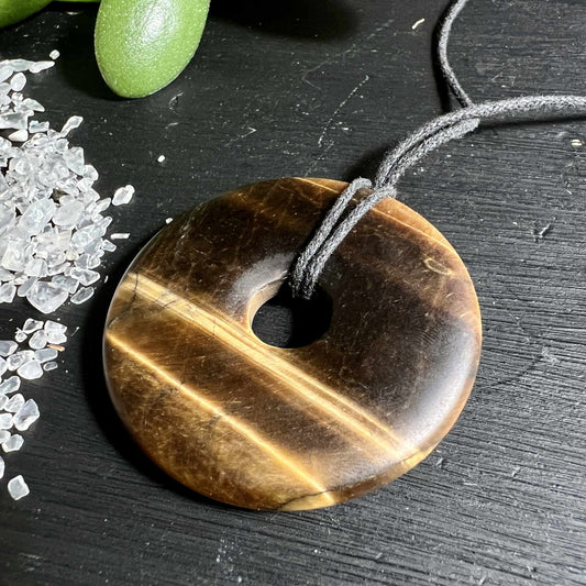 Matter Tigerauge Donut 50mm mit samtiger Oberflaeche neben Bergkristall